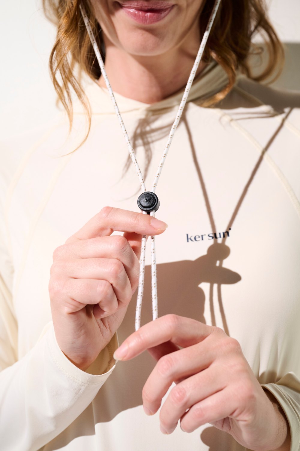 Femme portant un pull anti-UV beige de Ker Sun, ajustement avec cordon, idéal pour activités extérieures.