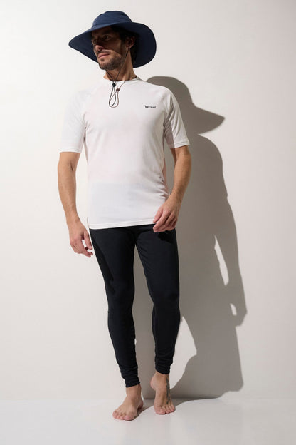 Homme en chapeau anti-UV bleu, t-shirt blanc UPF 50+ et leggings noirs, idéal pour la protection solaire lors d'activités en extérieur.